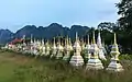 Tombes blanches et dorées en enfilade dans un cimetière bouddhiste au lever du soleil, avec les montagnes karstiques de Vang Vieng.