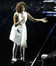 la chanteuse en blanc chantant dans un micro en bord de scène, l'autre bras écarté