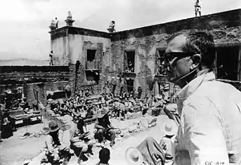 Le réalisateur Sam Peckinpah, au premier plan, est photographié dans la cour d'une hacienda en ruine remplie de figurants.