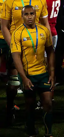 Portrait en pied d'un joueur de rugby en tenue jaune, avec une médaille autour de son cou