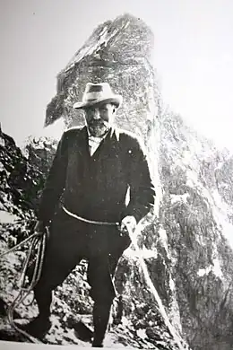 Photo en noir et blanc d'un homme tenant une corde avec une montagne en arrière-plan.