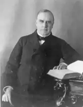 McKinley assis à un bureau devant un livre ouvert.