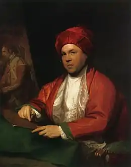 Peinture en couleurs. Un homme en vêtements et coiffe amples rouge et blanc est assis sur un fauteuil en velours vert. De trois-quarts, il regarde vers le spectateur avec une pointe sèche à la main droite, qui est posée sur une plaque de cuivre, qu'il tient avec sa main gauche.