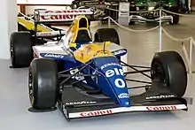 Photographie d'une monoplace de Formule 1 bleu foncé et jaune, exposée dans un musée, vue de face.