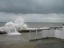Une grande vague s'abat sur la plage. Des terrasses sont inondées.