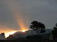 Sur un fond nuageux un rayon de Soleil perce au-dessus d'une montagne.
