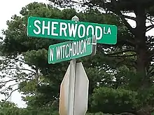 Plaque de rue indiquant « Sherwood La » dans une direction et « N Witchduck Rd » dans l’autre, en lettres blanches sur fond vert.