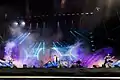 Photo en couleur d'un groupe de musique sur une scène, les lumières des projecteurs sont bleues et violettes
