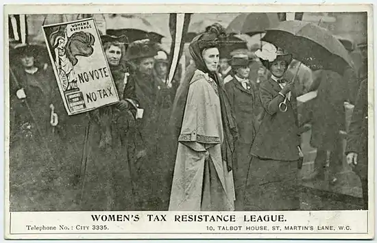 Clemence Housman est en gris au milieu de femmes habillées en sombre. À côté d'elle, une femme brandit une affiche représentant Minerve prête au combat, avec écrit « No Vote No Tax » et, sur son piédestal, Women's Tax Resistance League.