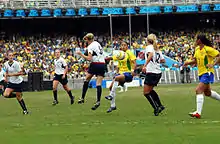 vue d'un match de football féminin, une joueuse en jaune contrôle le ballon devant deux adversaires en blanc.