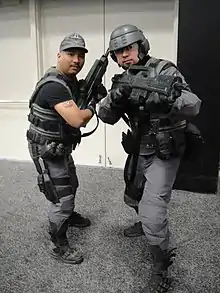 Deux hommes en tenue grise avec des mitraillettes.