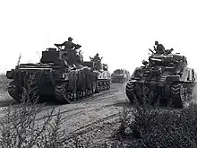 Photo en noir et blanc de chars d'assaut en mouvement sur un chemin de terre