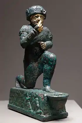 Statuette en métal d'un homme barbu agenouillé la main levée portée devant sa bouche.