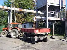 Tracteur rouge avec une remorque de petite capacité placée sous la goulotte d'un silo de laquelle tombe de la drêche.