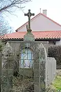 La croix de la Brunetterie est une croix en fonte pleine pose sur un socle dont la niche abrite une statuette de la Viergeentourée d'un muret