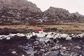 Une croix peinte en blanc sur un rocher et une montagne en arrière plan.