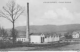 Photo noir et blanc d'une usine surmontée d'une haute cheminée.