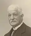 Photographie noir et blanc en buste d'un homme en costume portant la moustache.