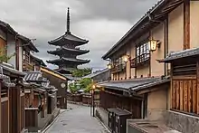Une rue qui descend, des maisons qui la bordent ; dans la perspective une pagode dresse ses étages dans un ciel gris. Par ci par là, quelque feuillages.
