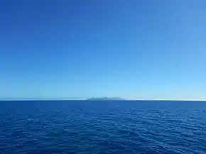 Étendue d'un océan, et une île en son centre au loin.