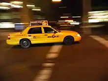 Taxi américain potographié la nuit, voiture de couleur jaune, sur un fond flou indiquant un déplacement du véhicule.