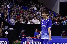Une joueuse de badminton, raquette en main, se tient debout devant une foule de spectateurs.