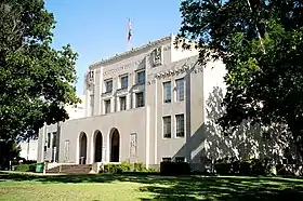 Vue partielle de la façade d'un bâtiment blanc bordée d'arbres.