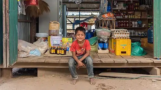 Jeune vendeur souriant, assis dans une épicerie à Don Som, Si Phan Don. Janvier 2018.