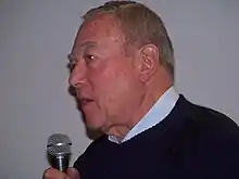 Homme âgé de profil parlant dans un micro.