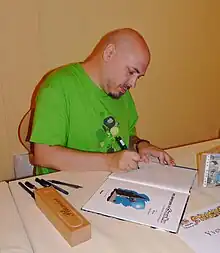 Photographie d'un dessinateur en train de dédicacer un album de bande dessinée.
