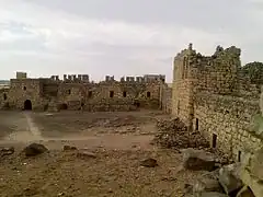 cour en terre battue, mur en pierre avec un édifice au centre