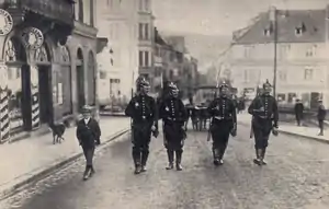 photographie en noir et blanc montrant quatre soldats allemands portant un fusil, à leur gauche un enfant