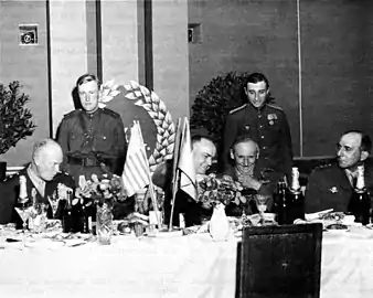 Photo noir et blanc de six hommes, dont quatre assis à une table, les deux autres derrière.