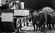 Photo noir et blanc d'un groupe de neuf officiers regardant un char d'assaut.