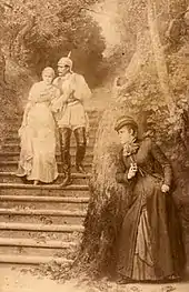 Gravure aux tons sépia montrant une femme en embuscade derrière un arbre avec un flacon, se préparant à vitrioler un couple (femme portant une robe et homme en tenue militaire avec un casque à pointe) descendant un escalier en extérieur.