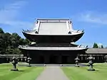 Wooden building with a metal plate covered roof and an enclosing pent roof giving it the appearance of a two-storied structure.