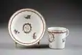 Tasse et soucoupe. Décor : médaillons avec au centre un buste de guerrier en armure antique, des fleurs, une guirlande tressée, une bordure dorée et glaçure.