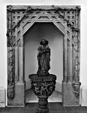 Photographie en noir et blanc d'un portail encadrant une statue de femme.