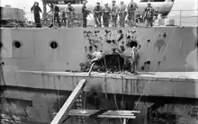 Photo en noir et blanc montrant des hommes accoudés à un bastingage regardant un gros trou dans la coque du navire.