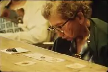 Une femme âgée, penchée vers une table, regarde de près 5 cartes à jouer alignées