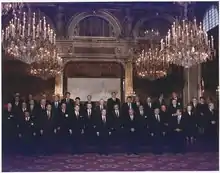 Photo en couleurs d'un groupe sur trois rangées au plafond des grands lustres au fond sur le mur une pancarte que laquelle est écrit CSCE, SOMMET DE PARIS, 19 au 20 juin 1990