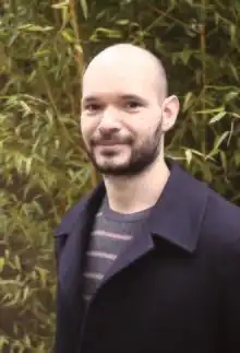 un homme chauve et barbu devant des bambous